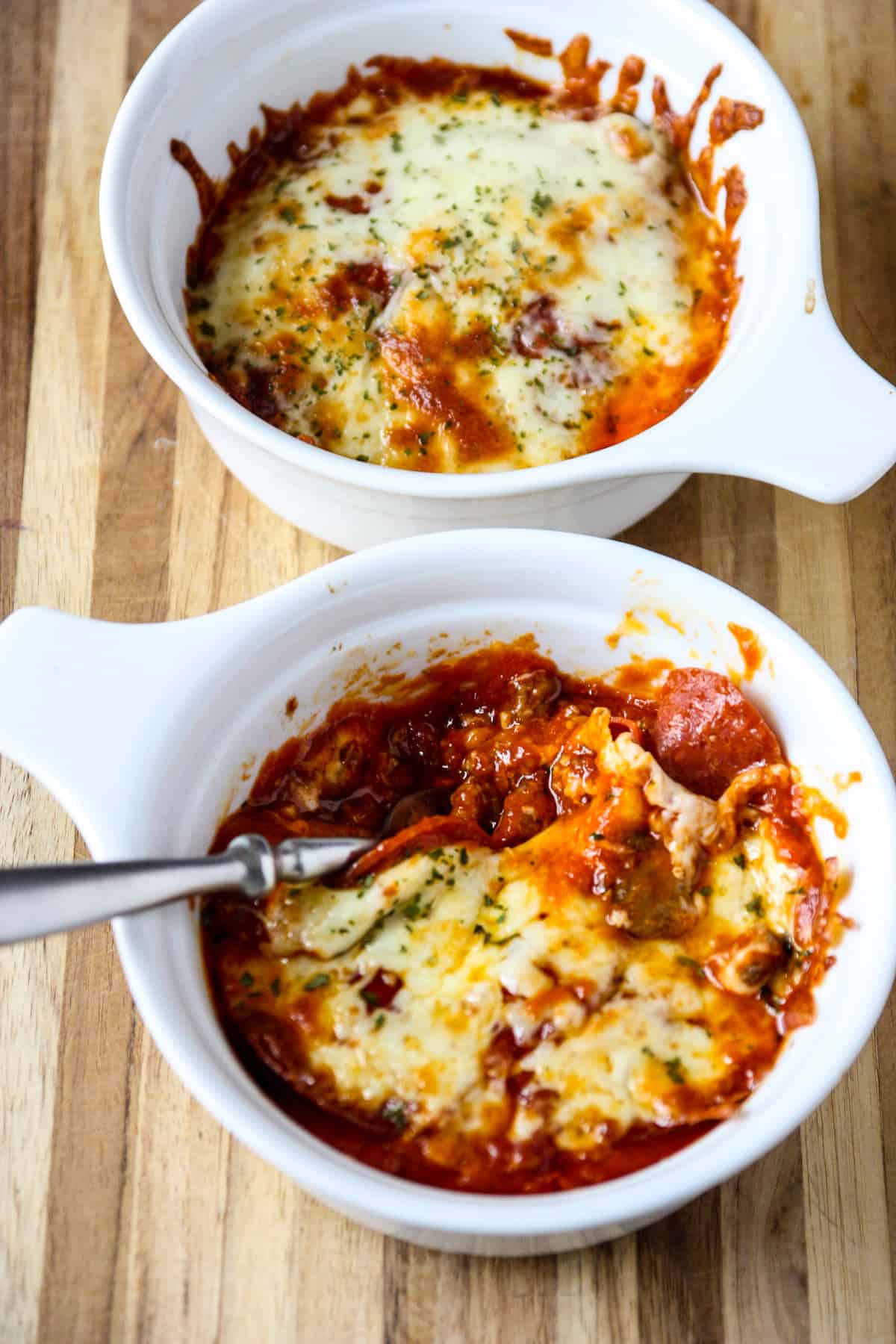 Two pizza bowls on a wooden cutting board.