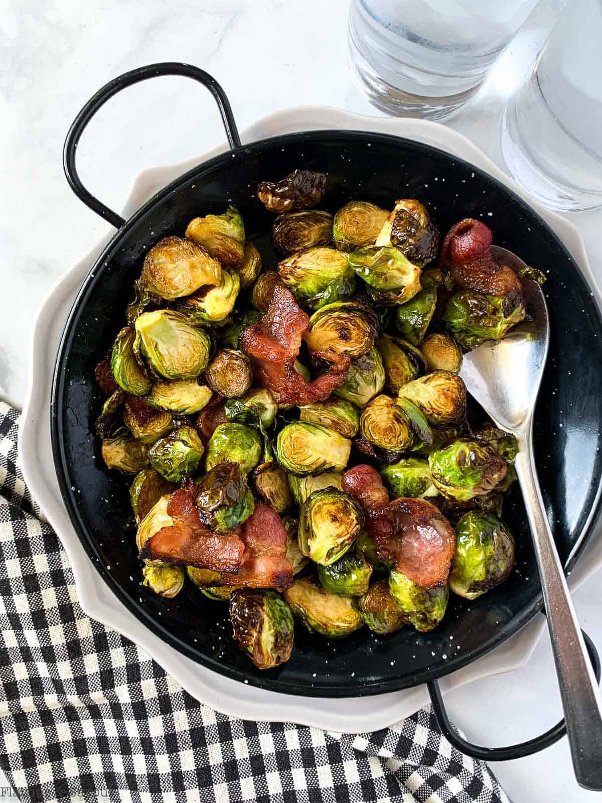 An air fryer basket filled with air fried brussels sprouts and bacon.