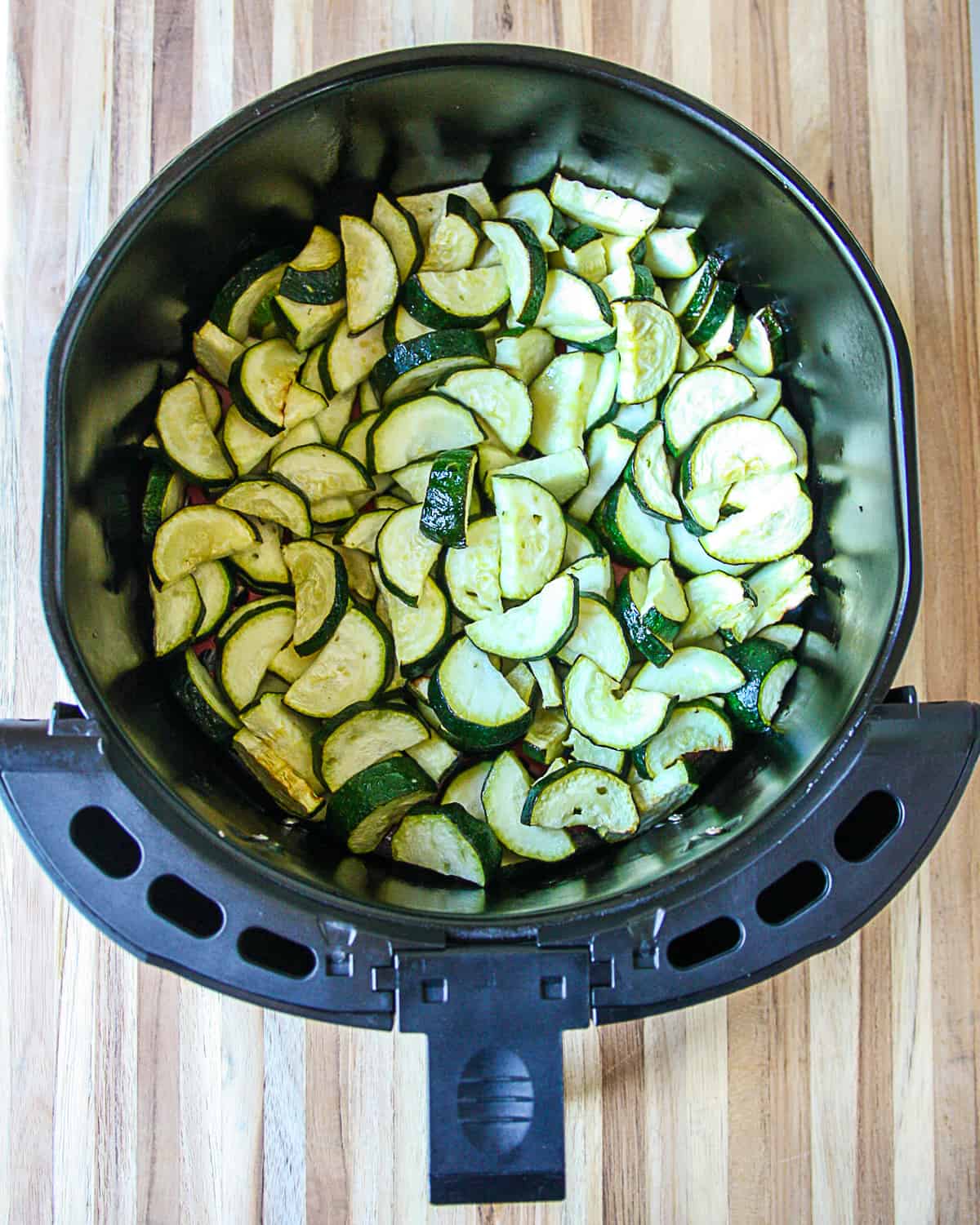 Cooked zucchini slices in an air fryer basket.