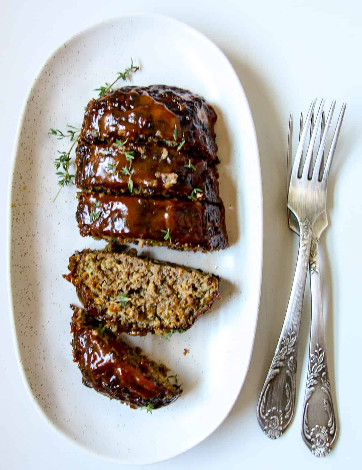 A sliced glazed air fryer meatloaf on a white plate next to two silver forks.