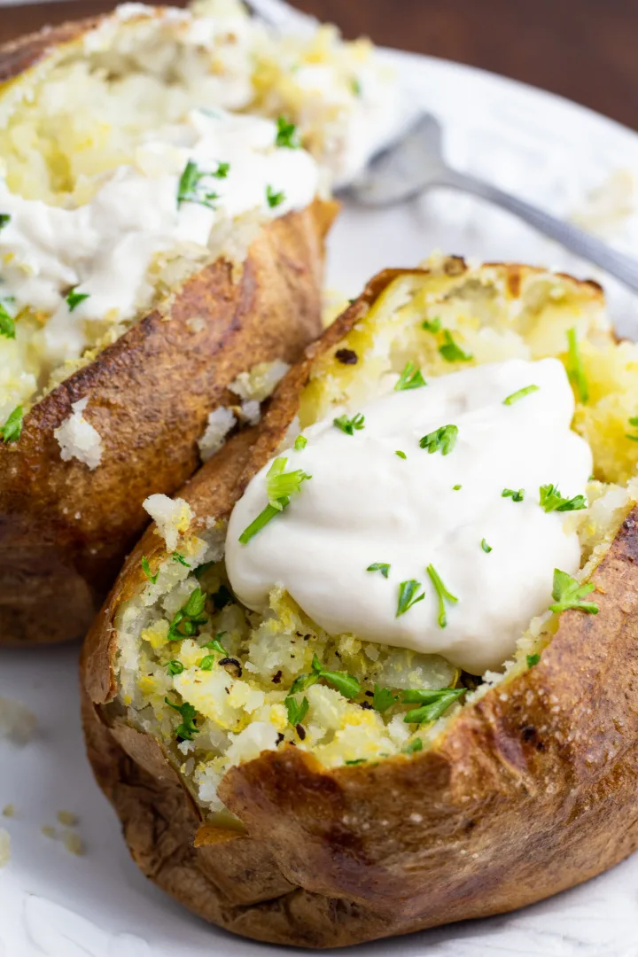 Two baked potatoes topped with butter and sour cream on a white plate.