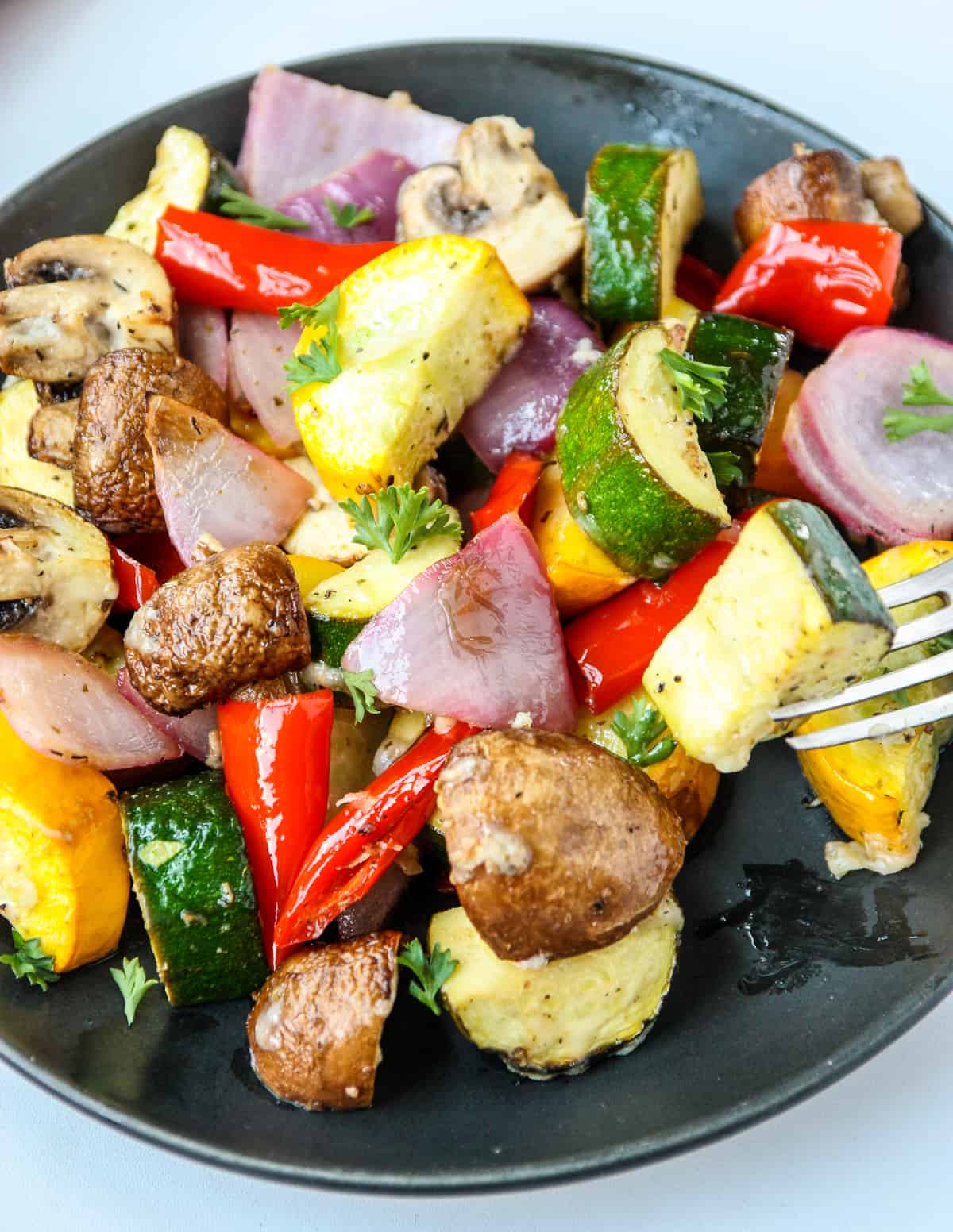 A black plate filled with air fryer roasted vegetables and a silver fork.