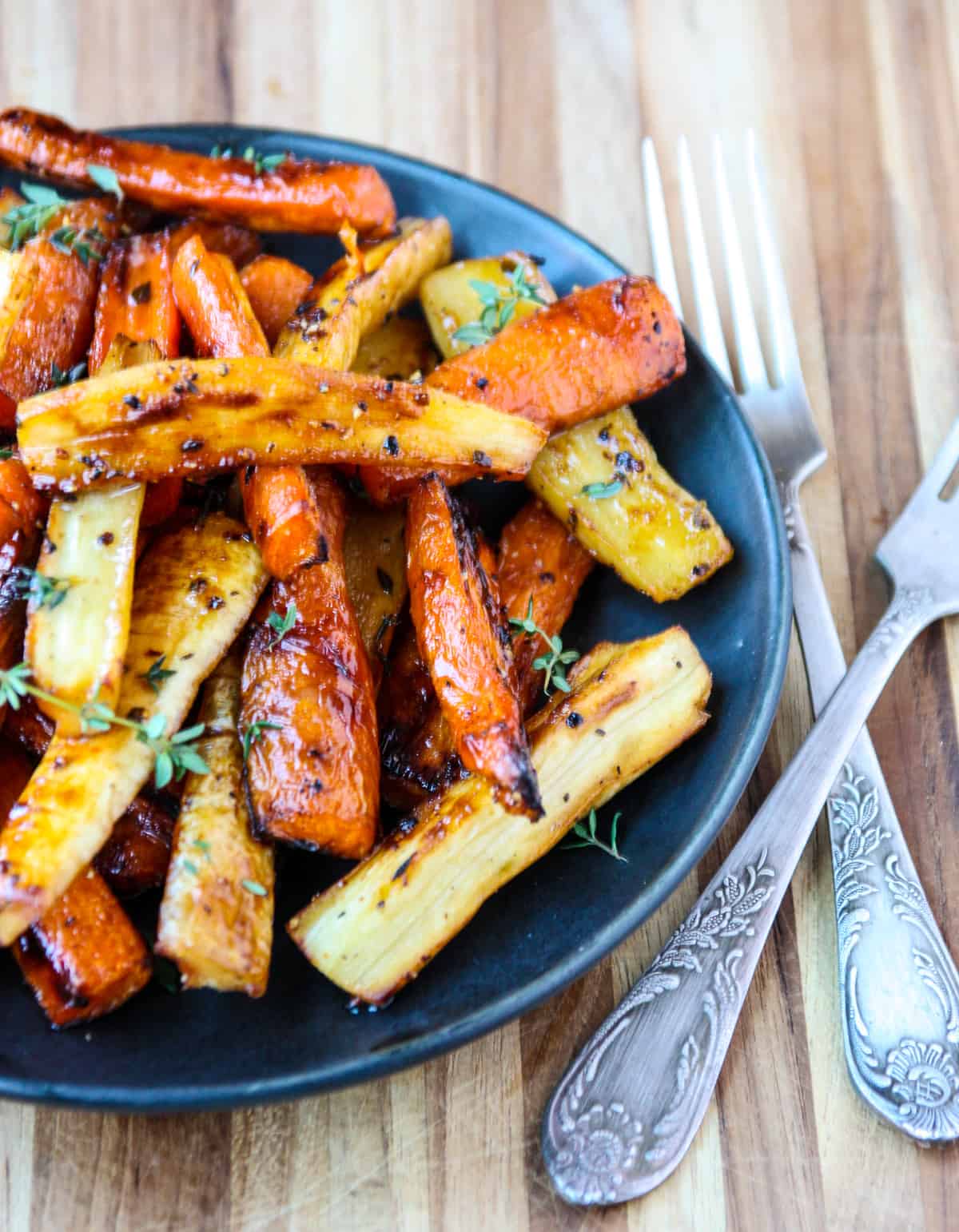The honey roasted carrots and parsnips being served on a plate with silver forks.