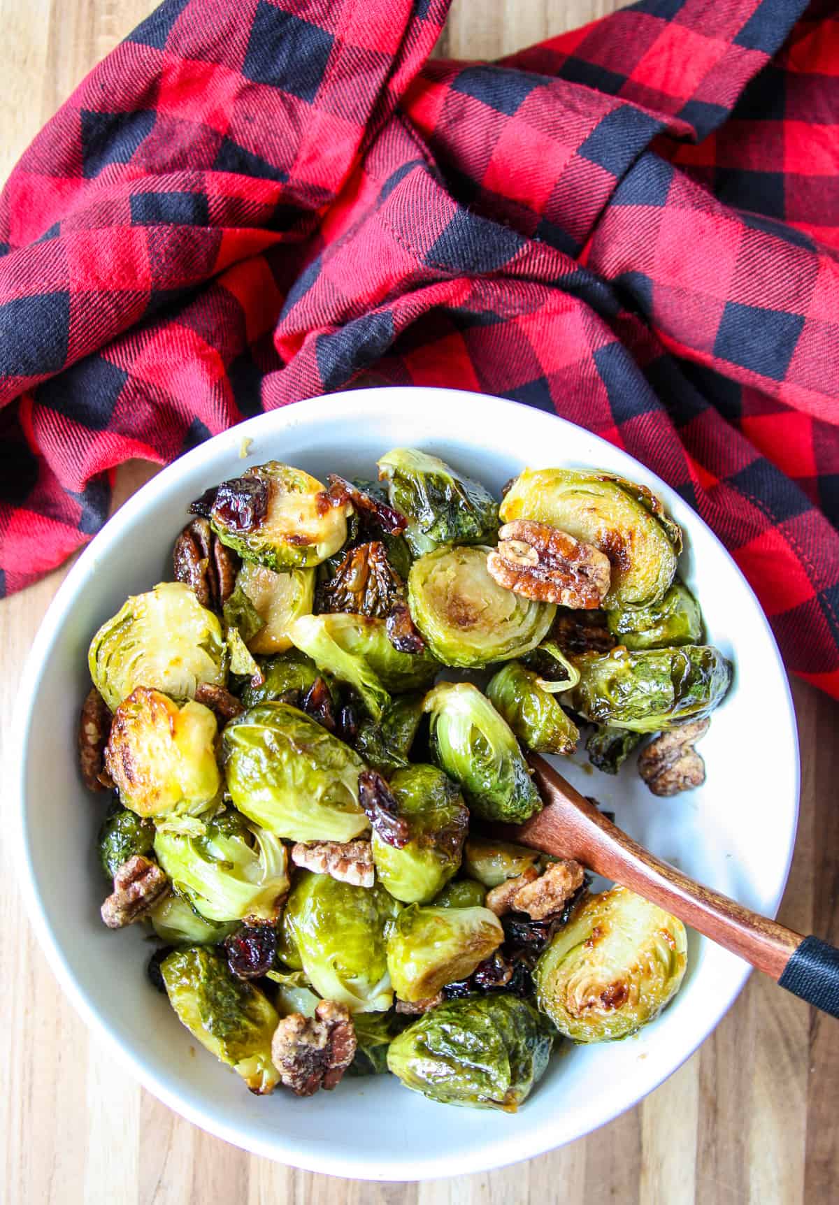 A bowl of brown sugar brussels sprouts with a wooden spoon.