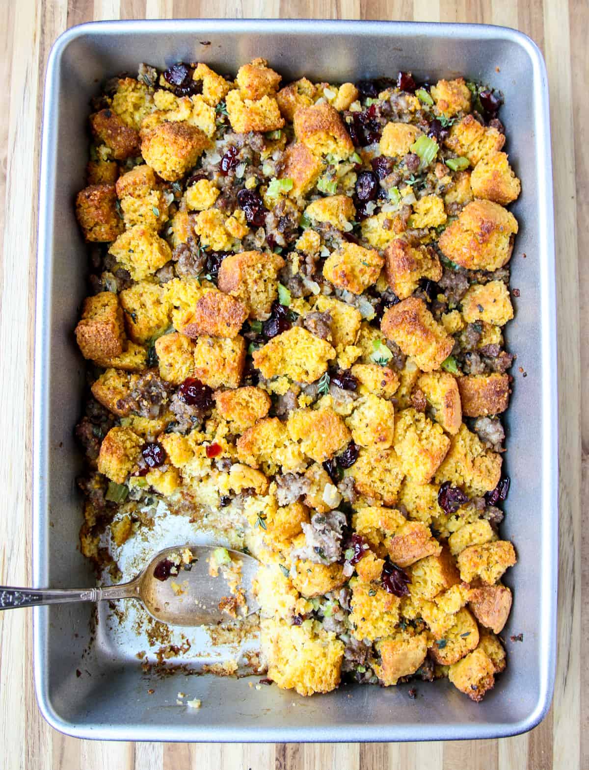 A silver spoon scooping out cornbread stuffing from a baking pan.