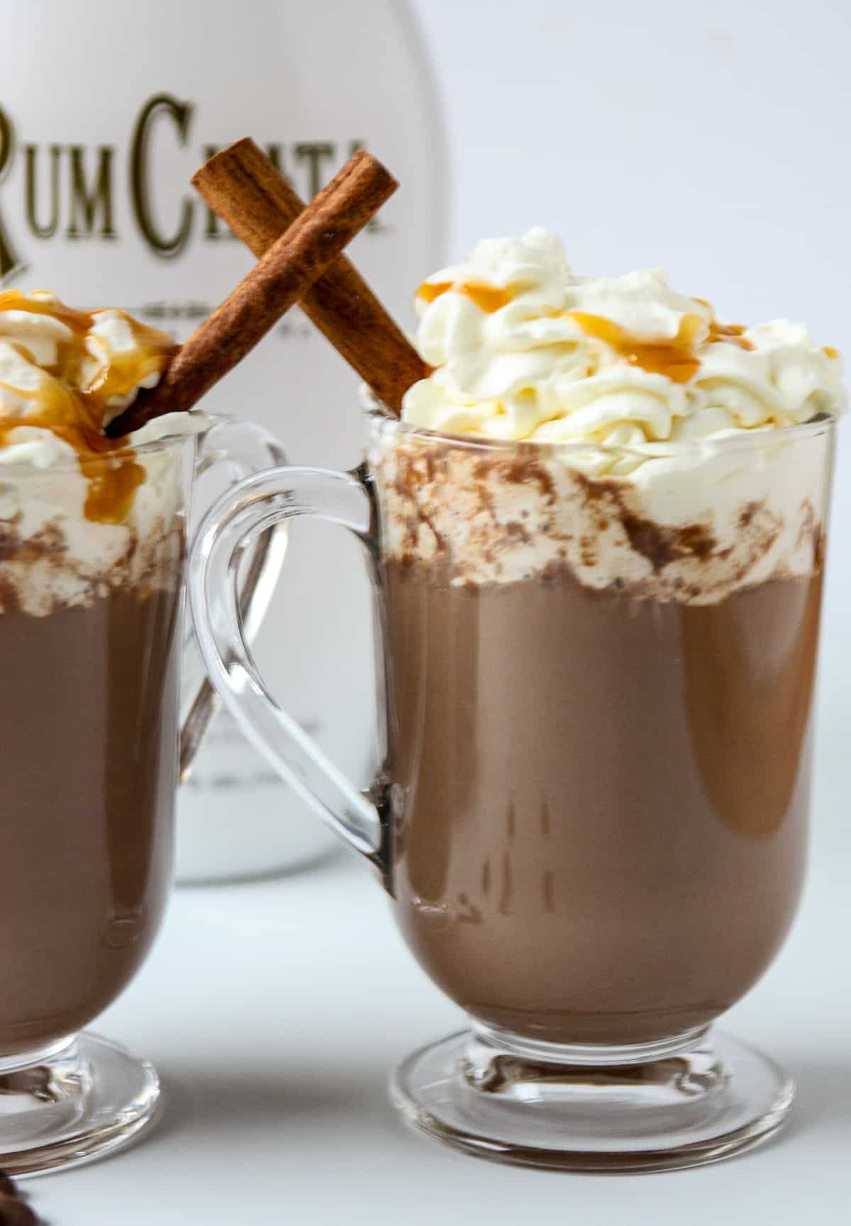 A bottle of RumChata behind two mugs of hot chocolate.