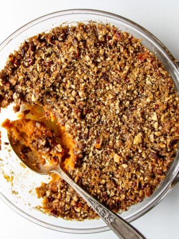 A serving spoonful of sweet potato crunch being taken from a casserole dish.