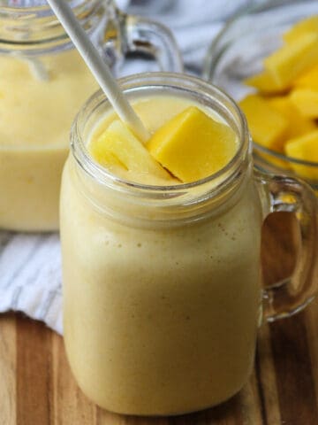Two glasses of mango pineapple smoothie with white paper straws.