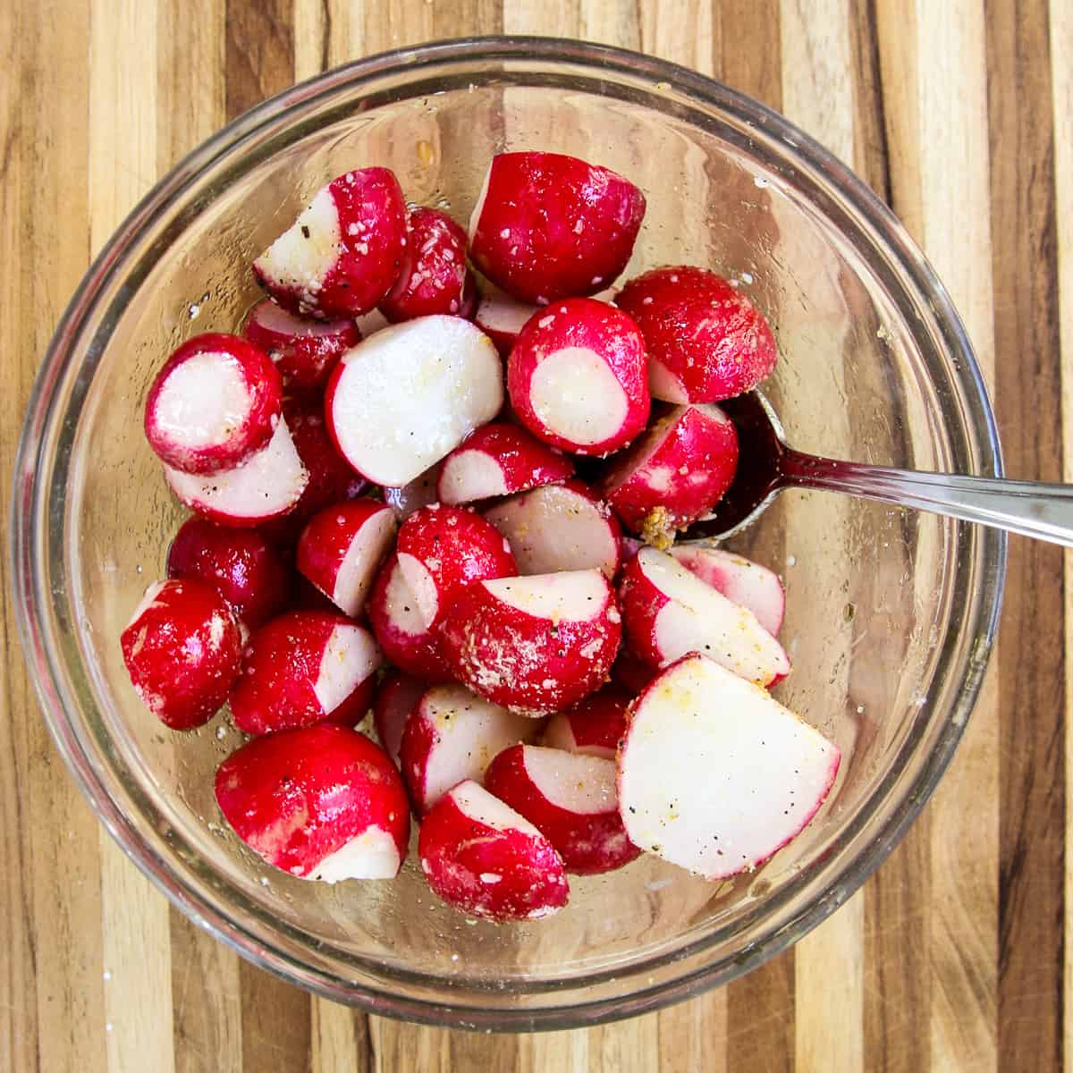 Sliced radishes in a glass bowl being tossed with oil and seasonings.