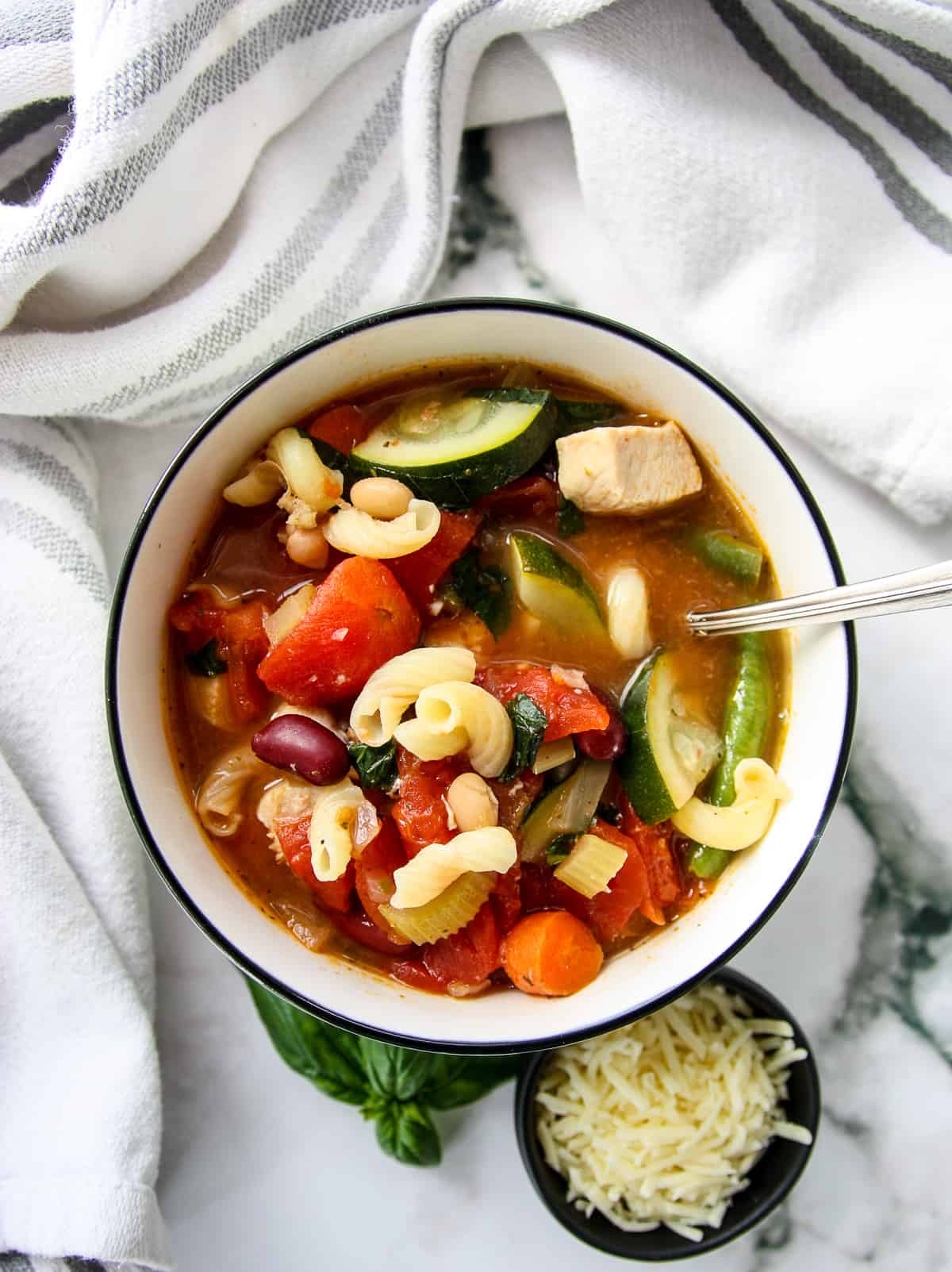 A bowl of chicken minestrone soup and a small dish of grated cheese.