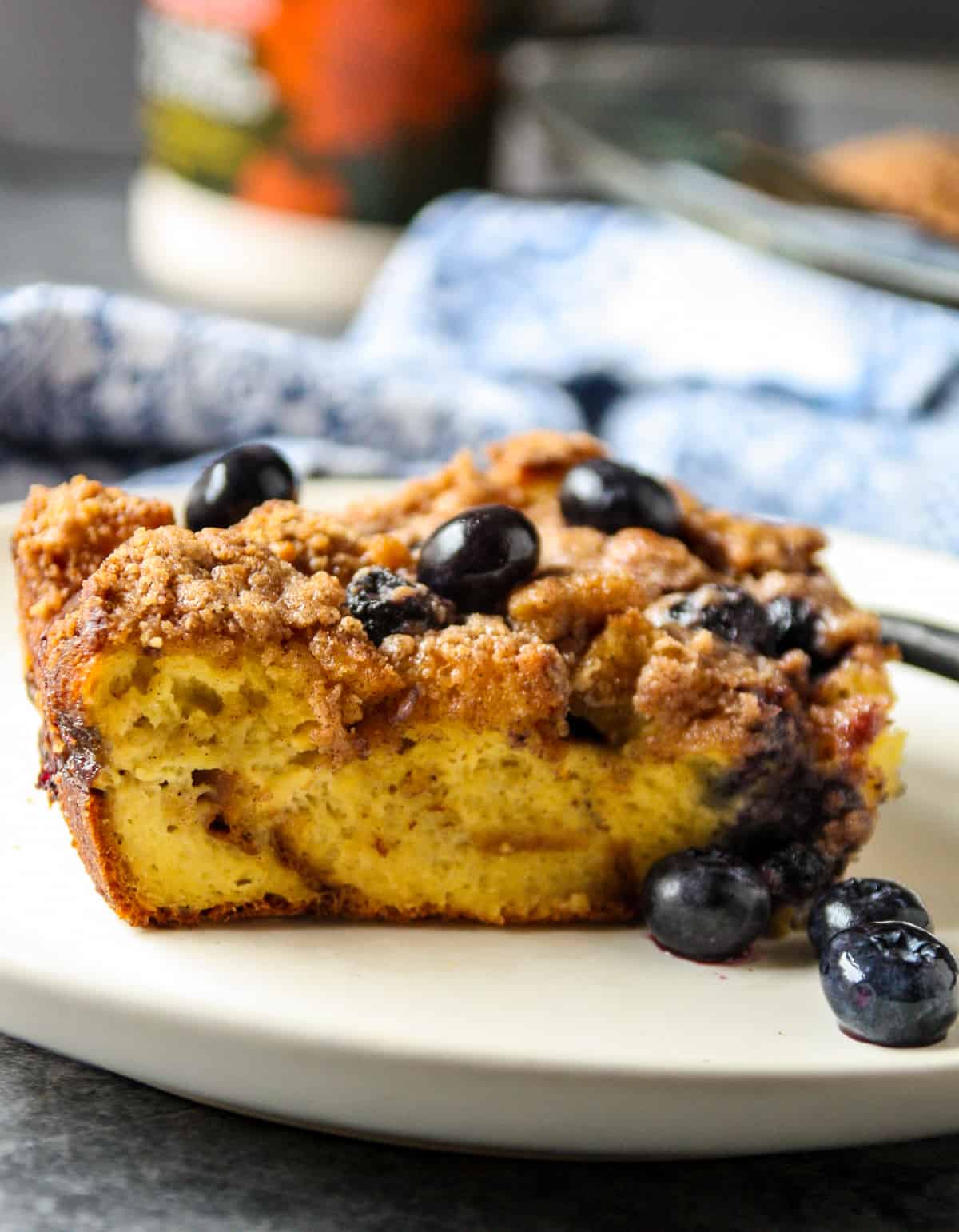 A brioche French toast casserole slice topped with blueberries on a white plate.