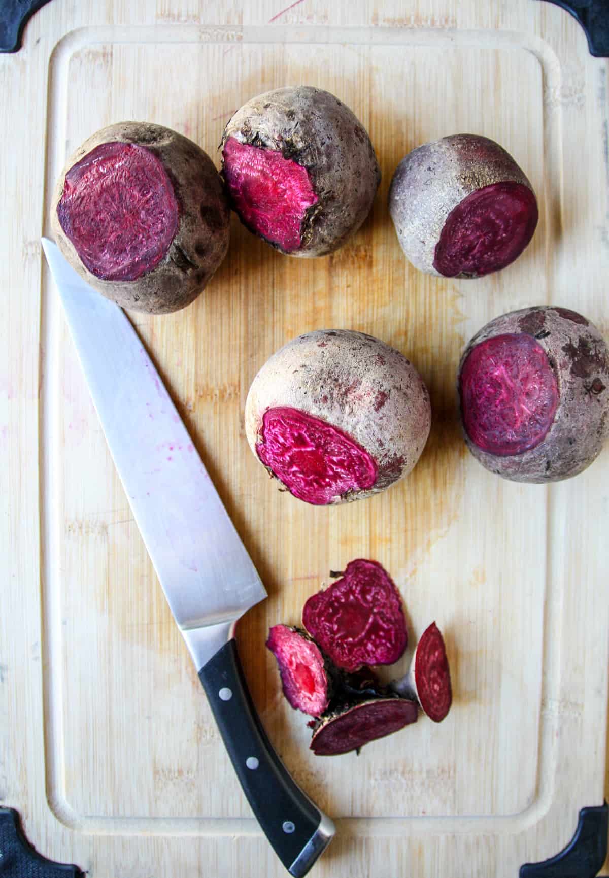 Raw beets on a cutting board with stem and tail ends sliced off.