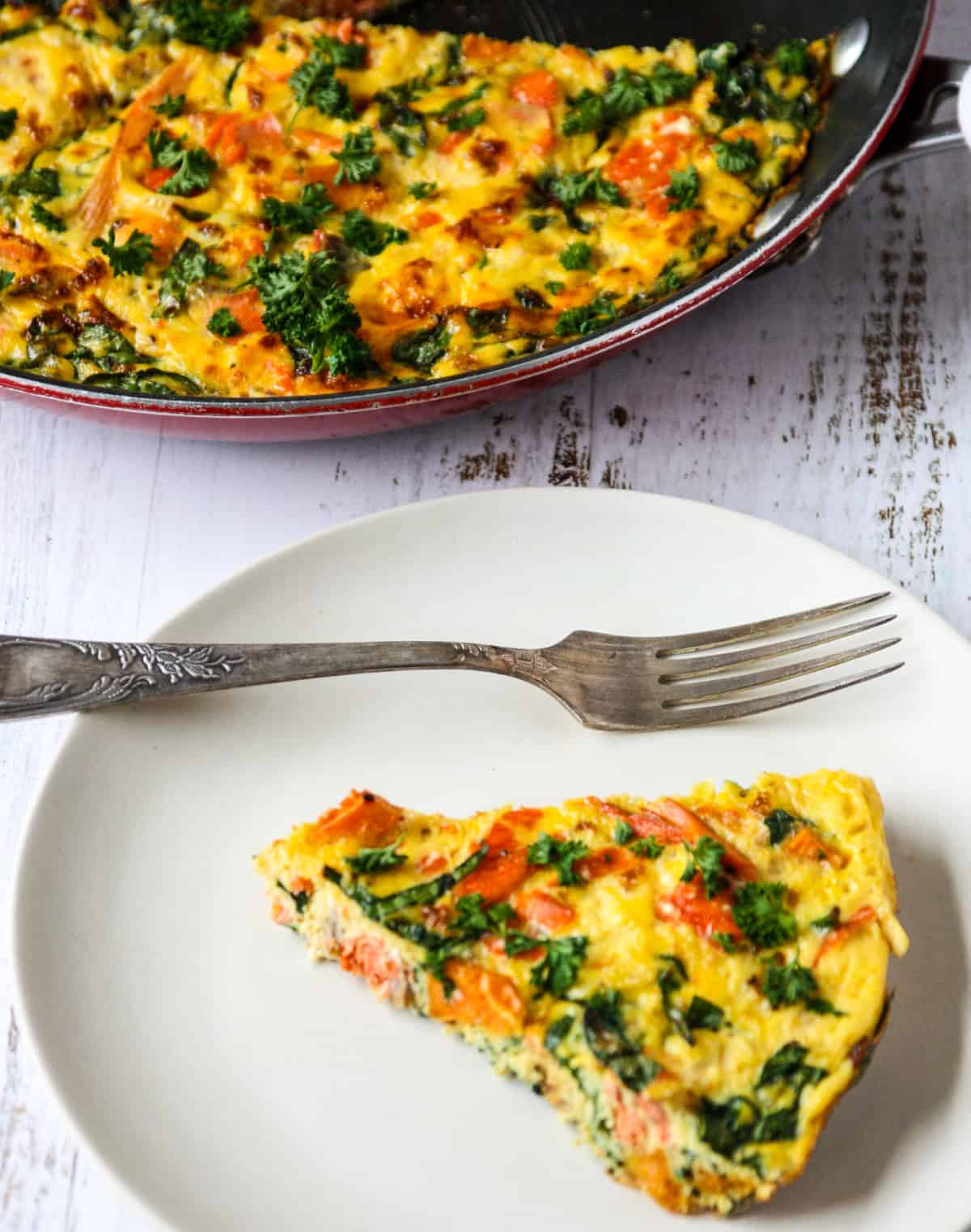 A pie-shaped slice of salmon frittata on a white plate.