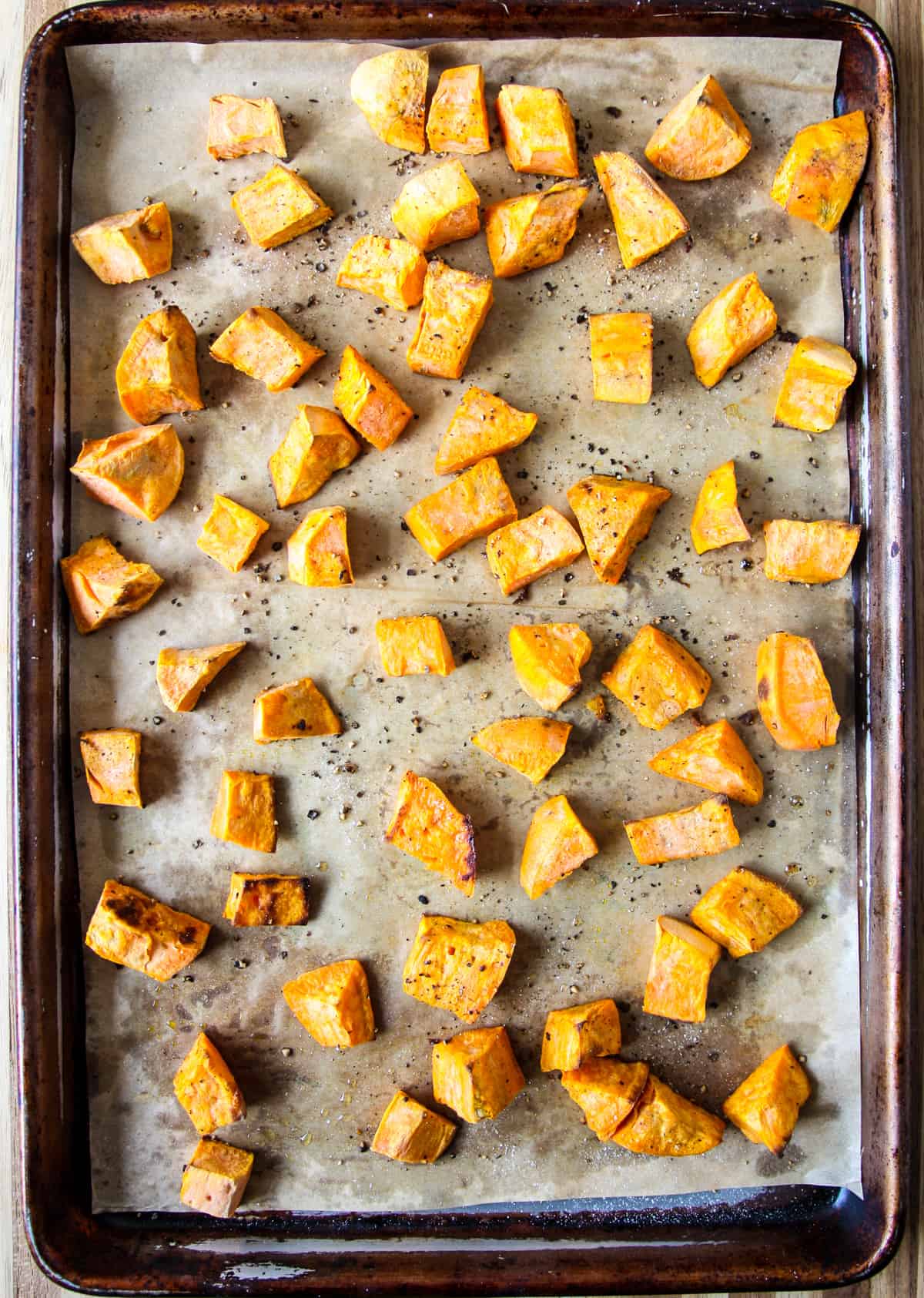 Cubes of roasted sweet potato on a parchment lined baking sheet.