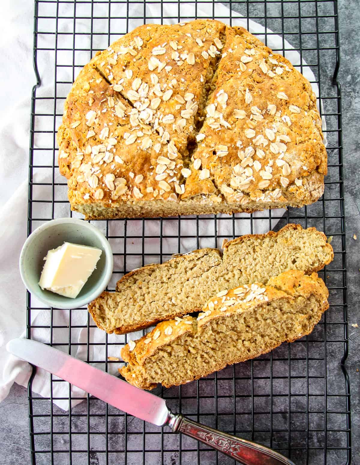 A round loaf of gluten-free Irish soda bread with two slices removed, and a small dish of butter.