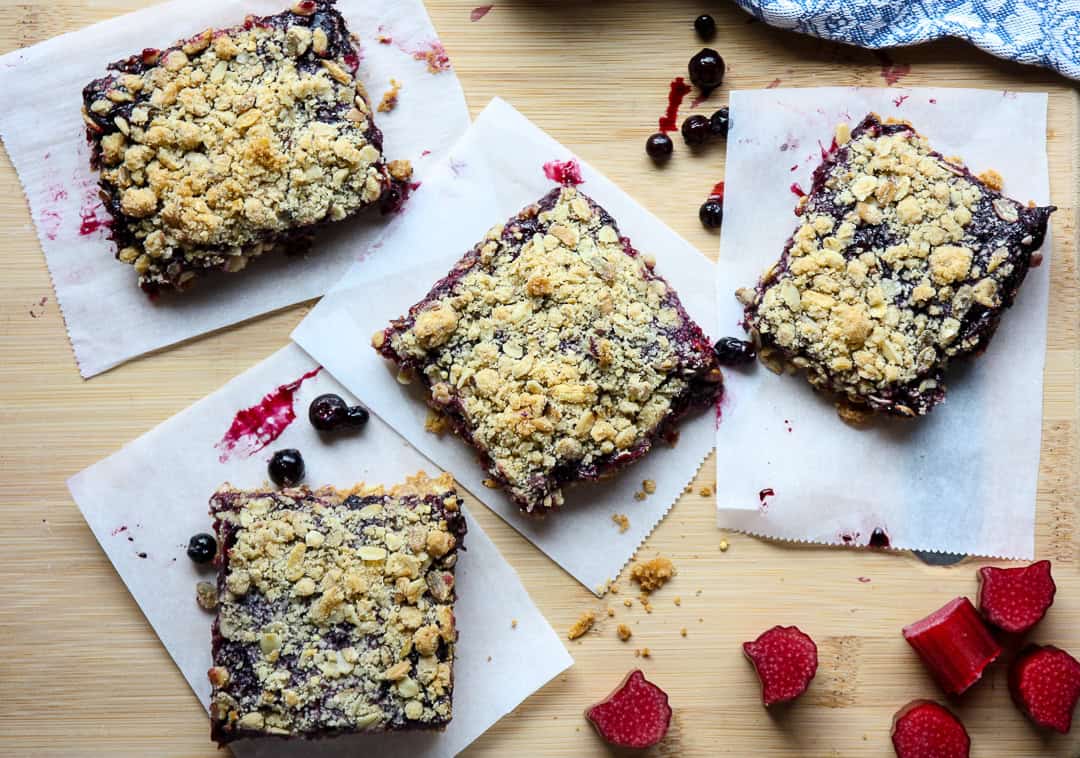 Four rhubarb blueberry oatmeal bars on parchment paper.