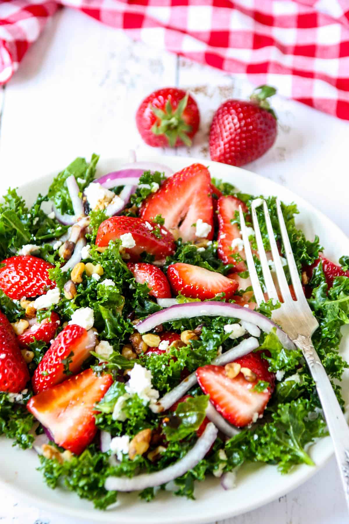Strawberry kale salad on a white plate with a silver fork.