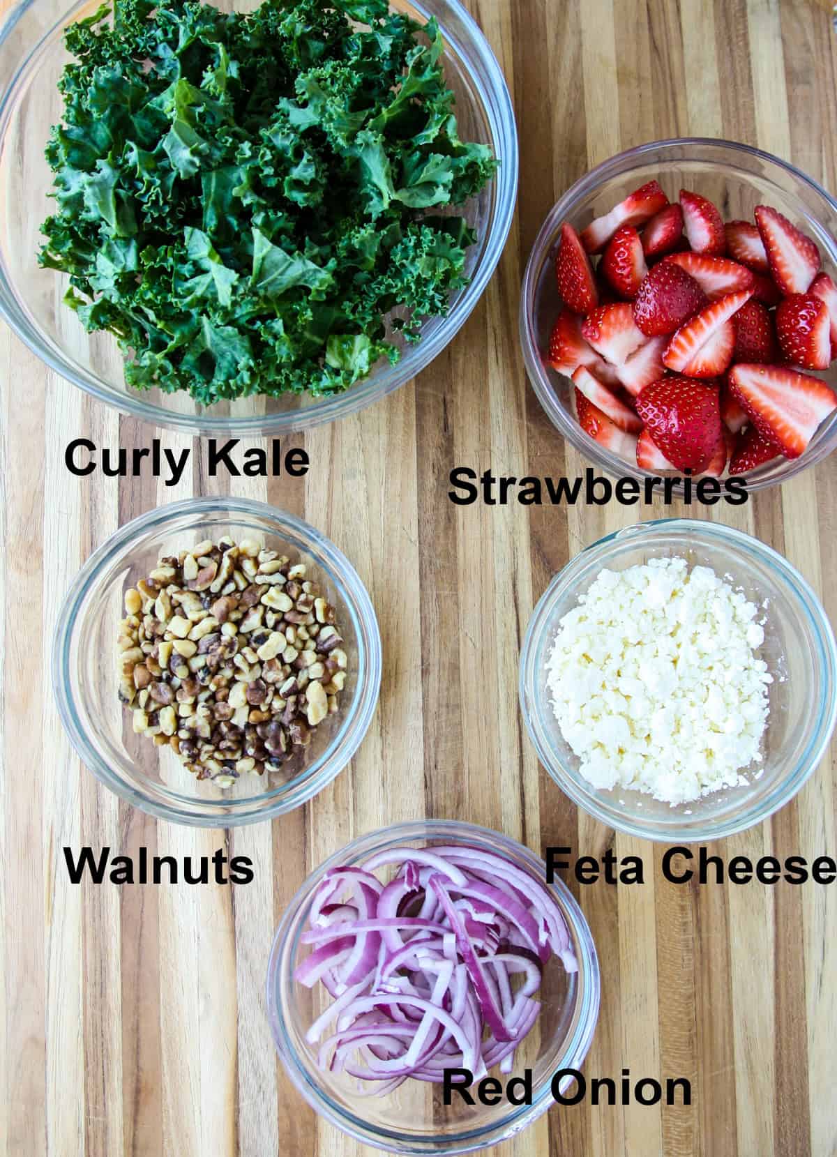 The salad ingredients in glass bowls on a wooden cutting board.