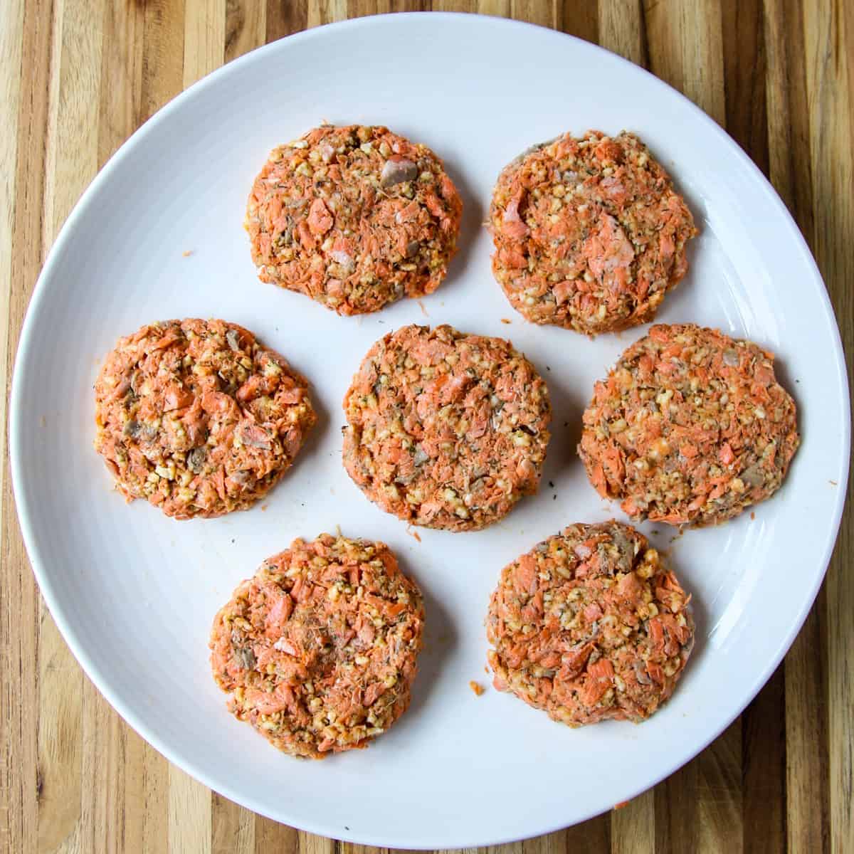 The formed salmon patties before being fried, on a white plate.
