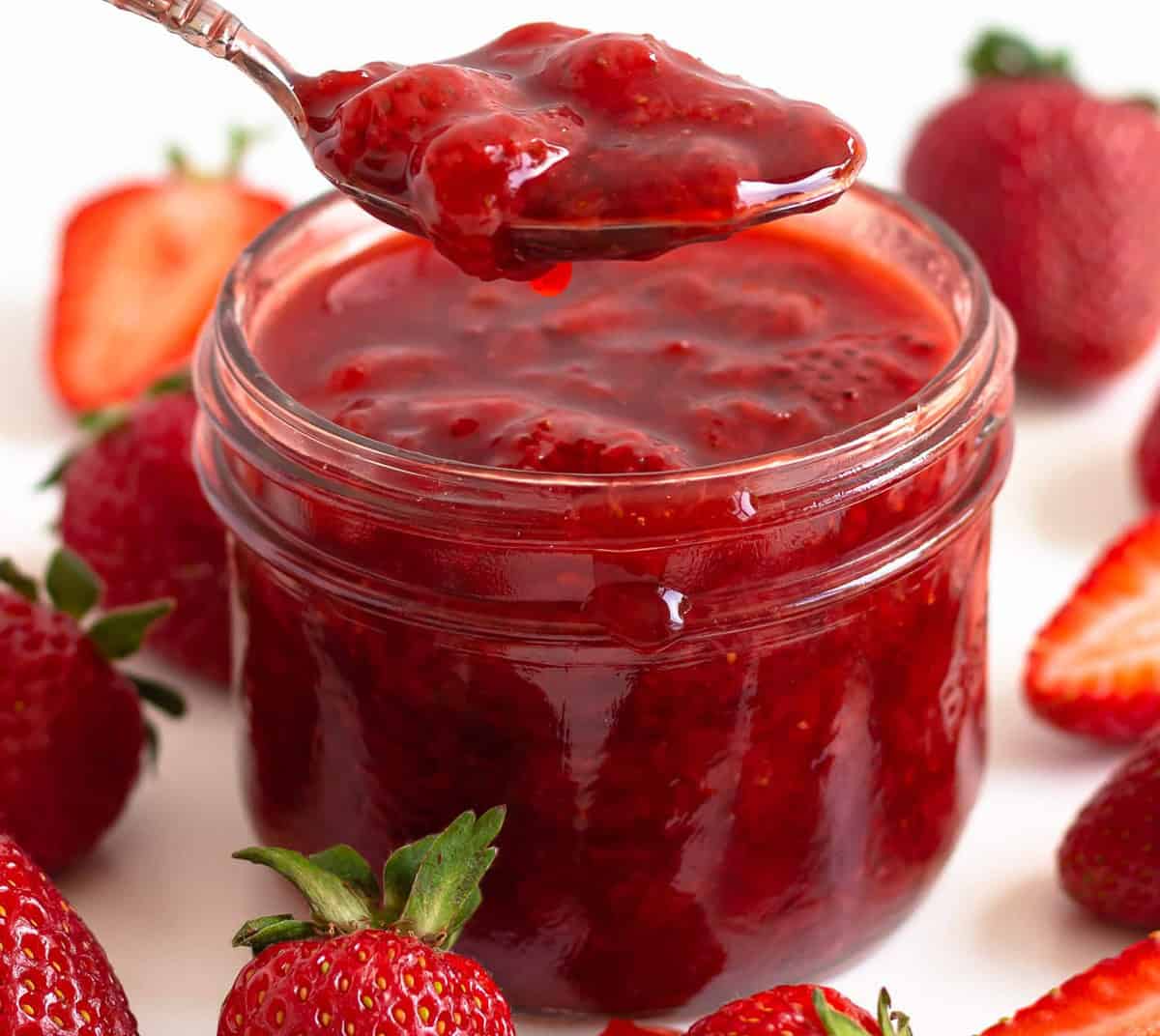 A jar of strawberry compote with a silver spoon.