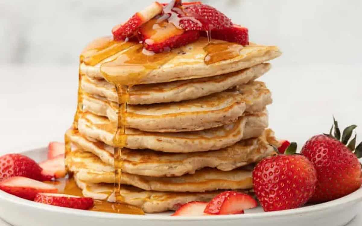 A stack of strawberry pancakes topped with syrup.