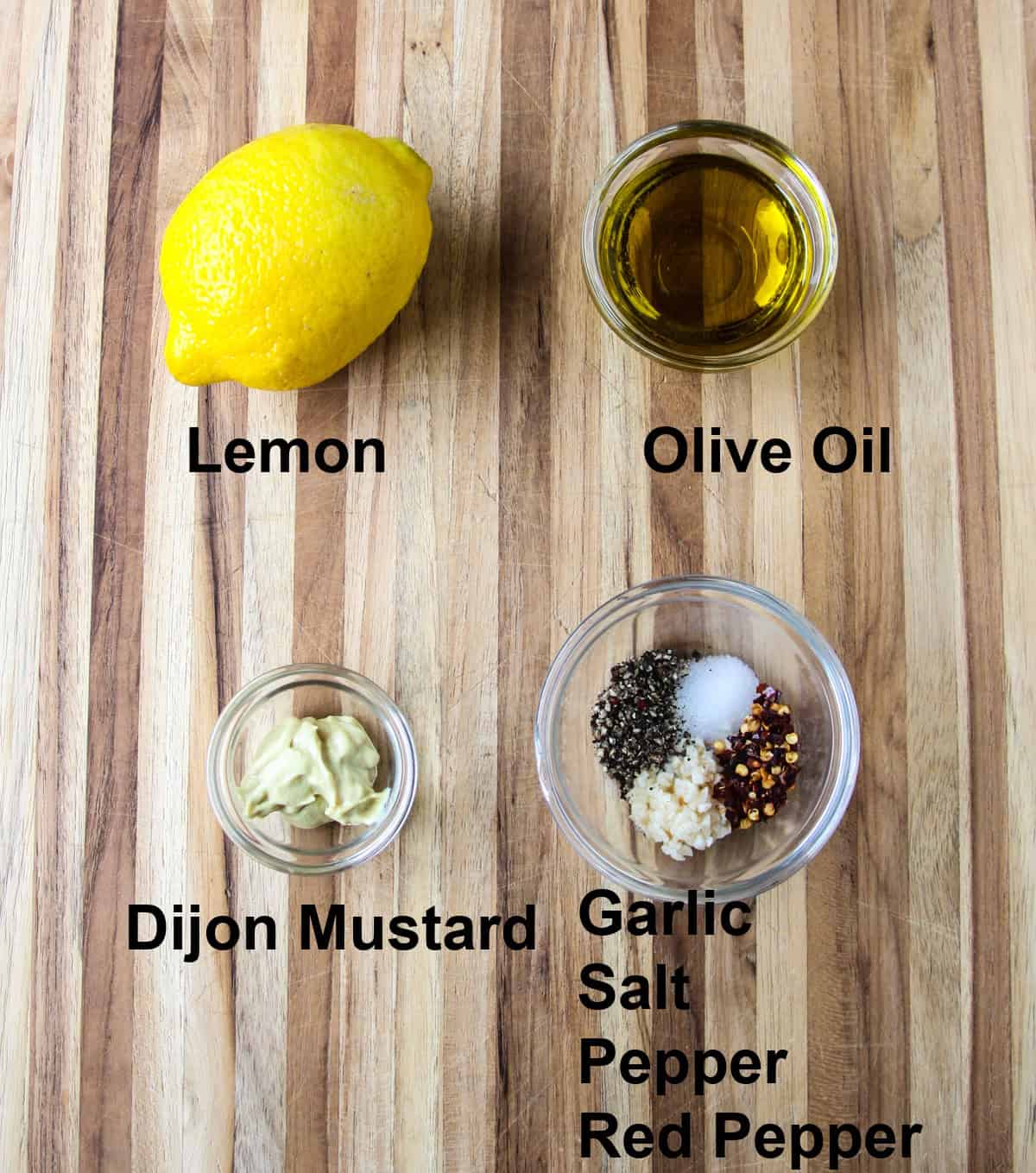 The ingredients for making the salad dressing, in glass bowls on a wooden board.