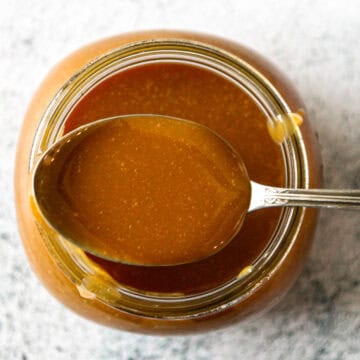 A spoonful of caramel candy sauce resting on the rim of a jar.