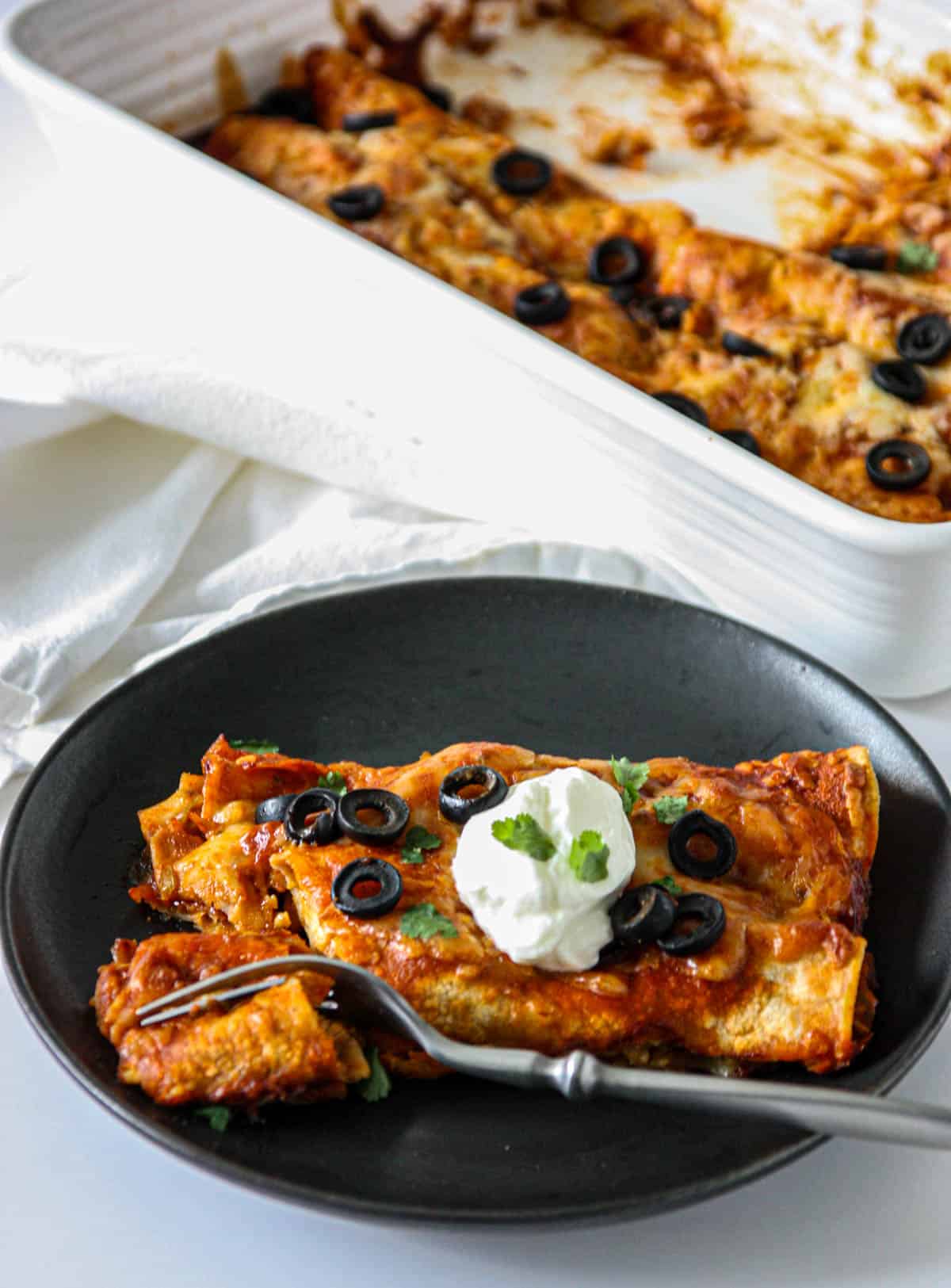 Two turkey enchiladas on a black plate with a fork.