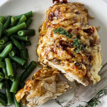 French onion chicken on a white plate with green beans.