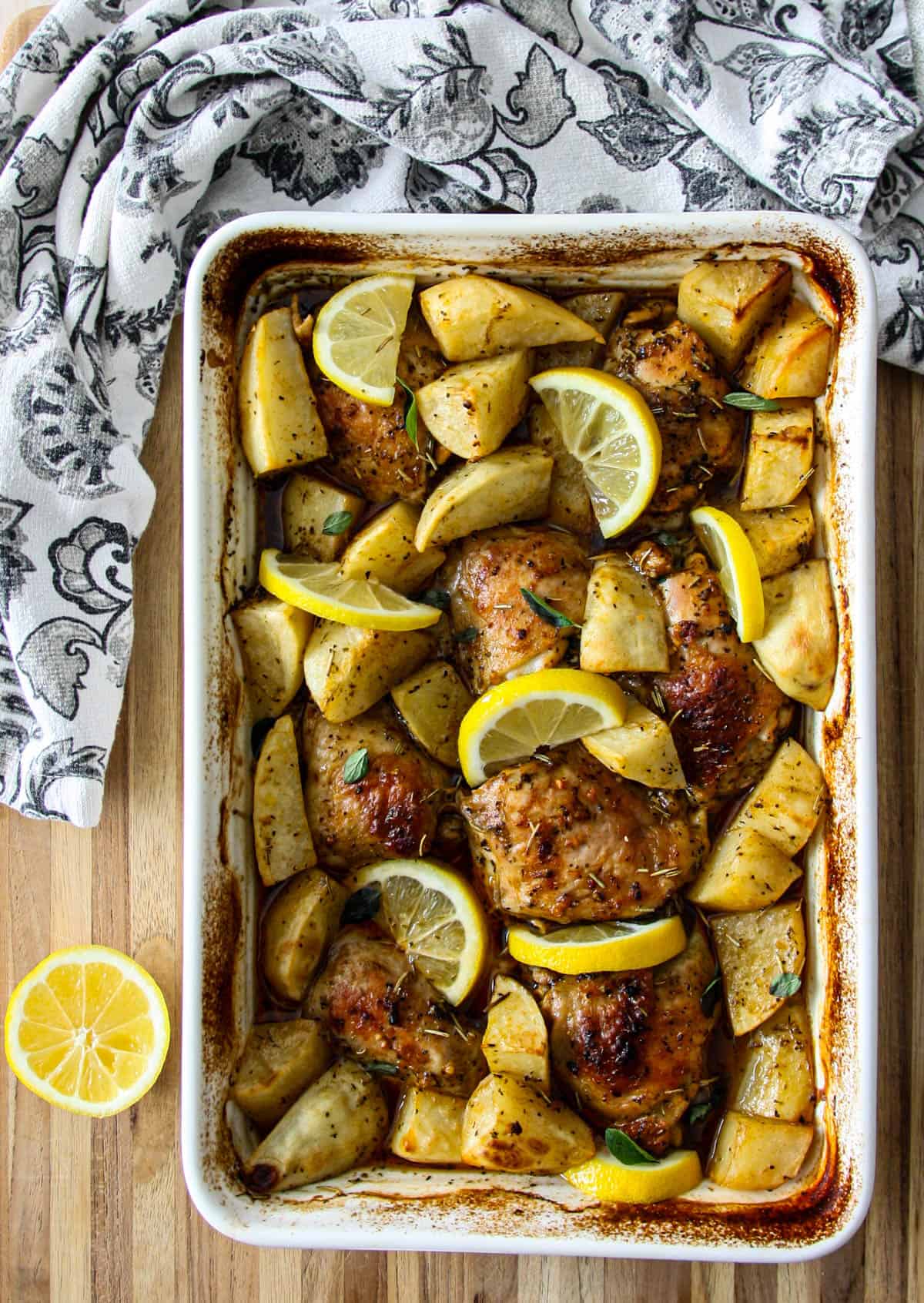 Greek lemon chicken and potatoes in a white baking pan.