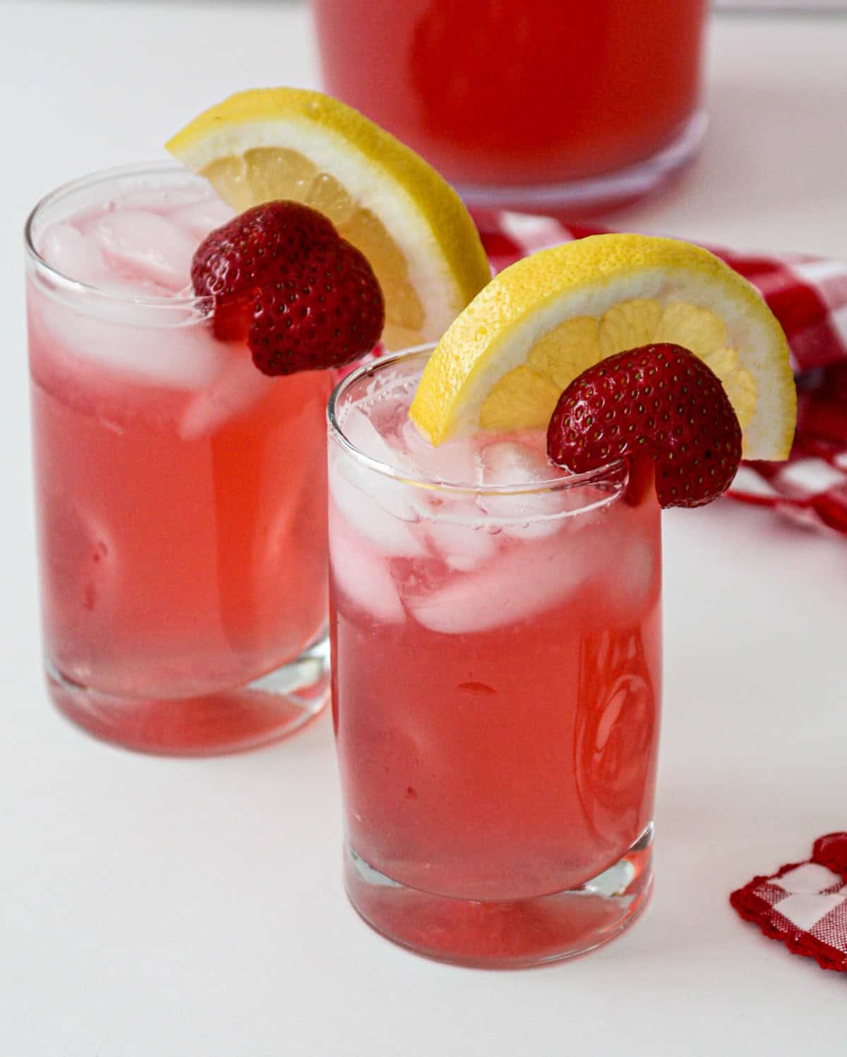 Two glasses of rhubarb lemonade, garnished with lemon and strawberry slices.