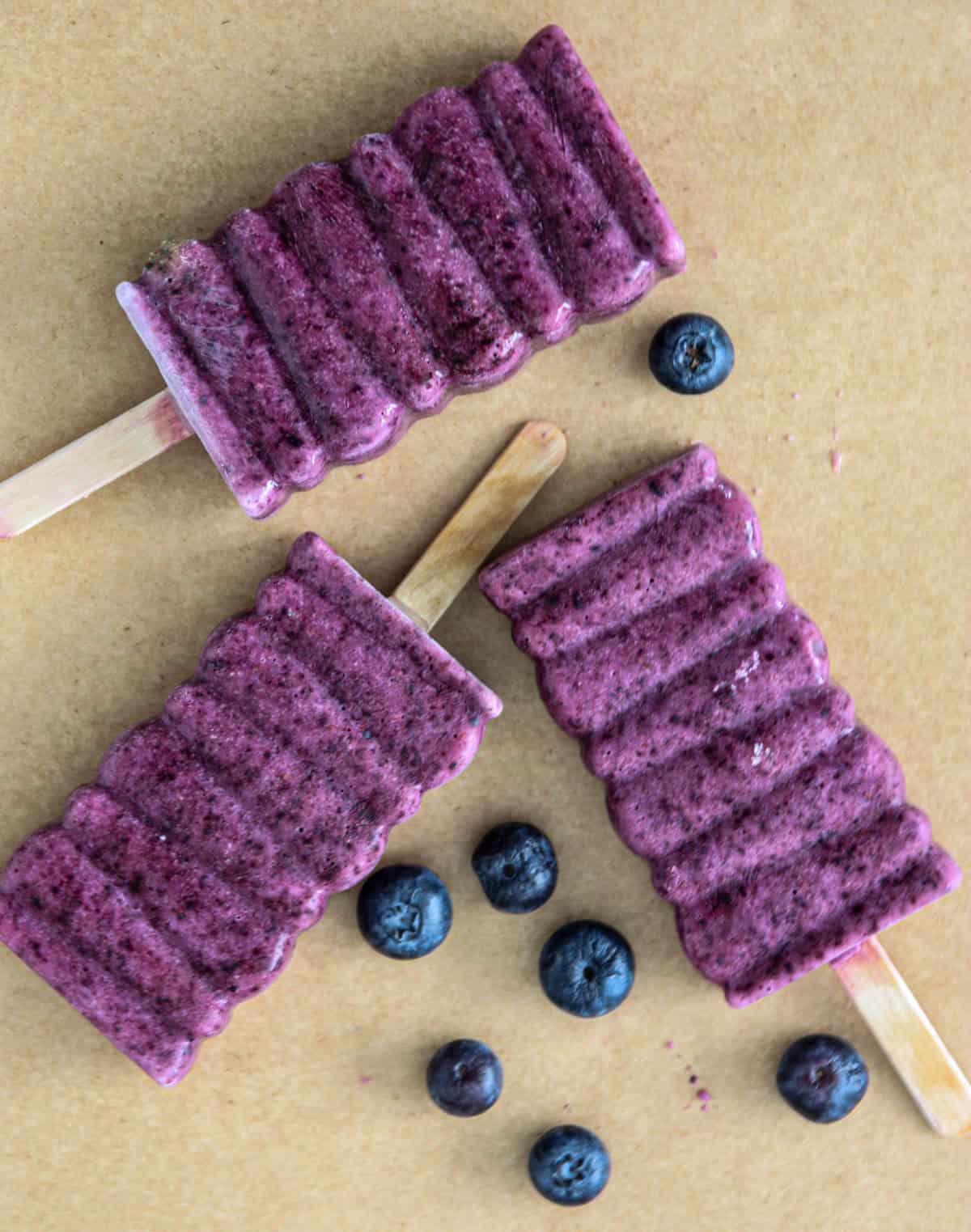 Three blueberry popsicles on wooden sticks.