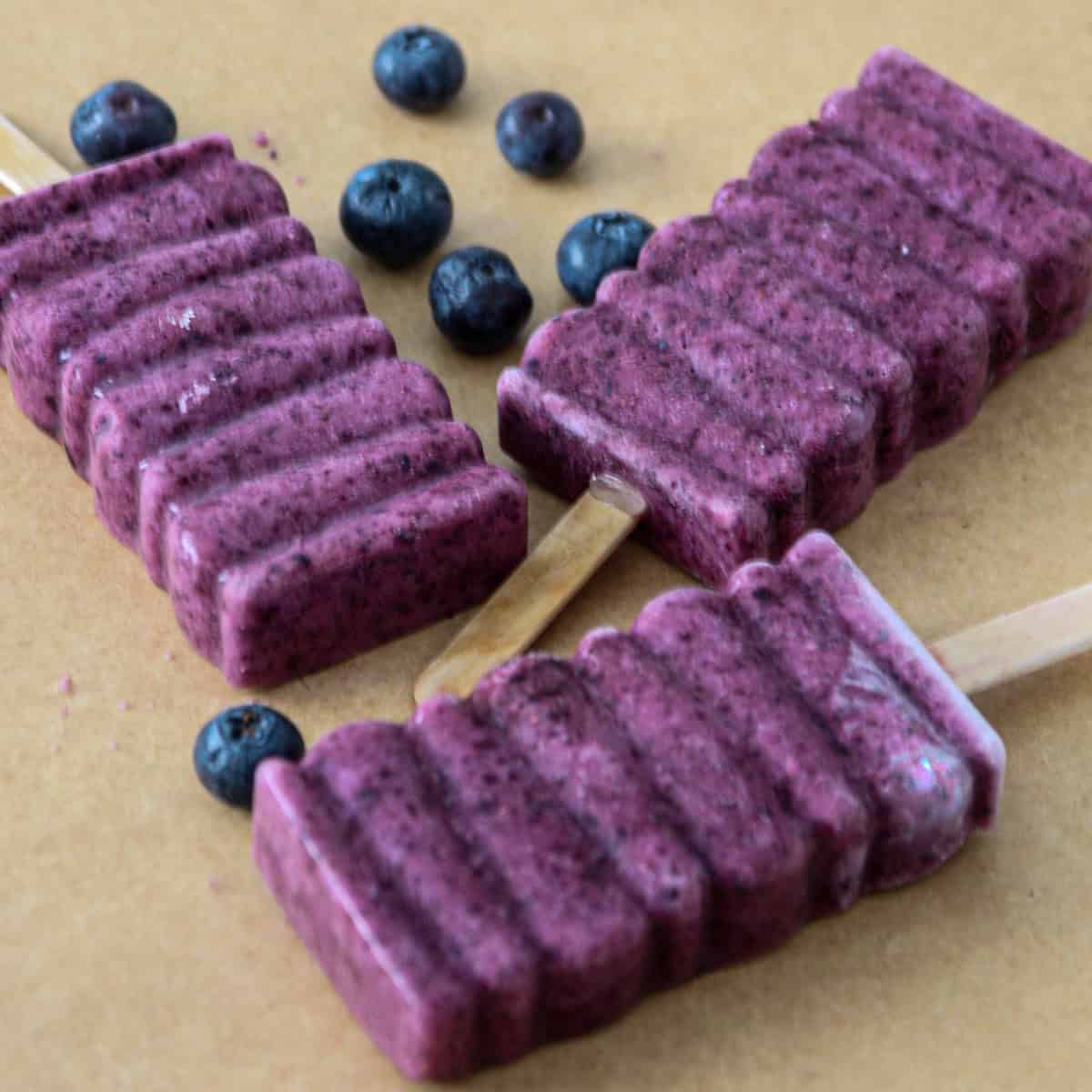 Three homemade blueberry popsicles on parchment paper.