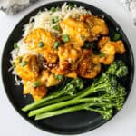 Bang bang chicken on a bed of rice on a black plate.