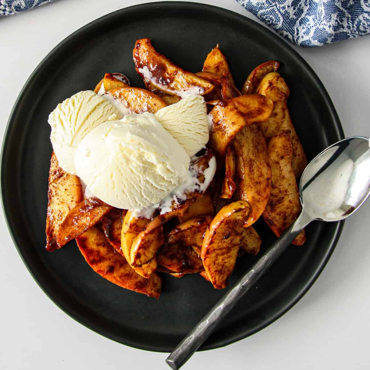 Air fried apple slices on a black plate, topped with vanilla ice cream.