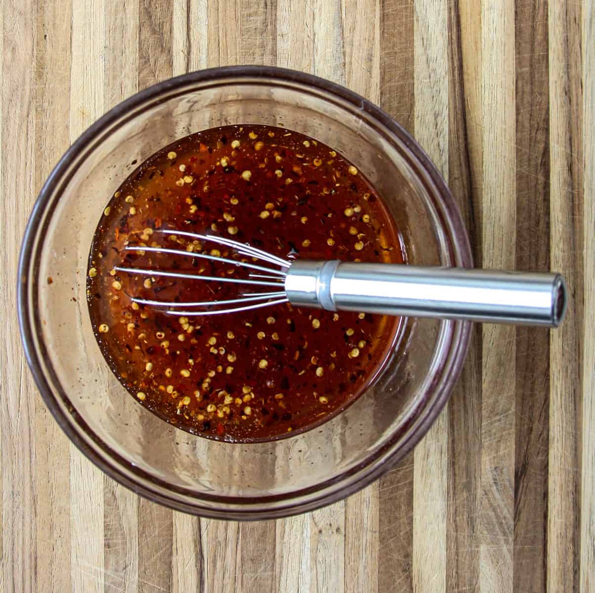 The ingredients for the hot honey recipe in a glass bowl with a wire whisk.